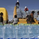 Men unload packs of water from a truck a