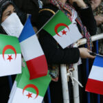 A woman holds Algerian and French flags as she waits for the arrival of France’s President Nicolas Sarkozy in Tipaza