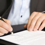 Business person signing a contract, focus on signature.